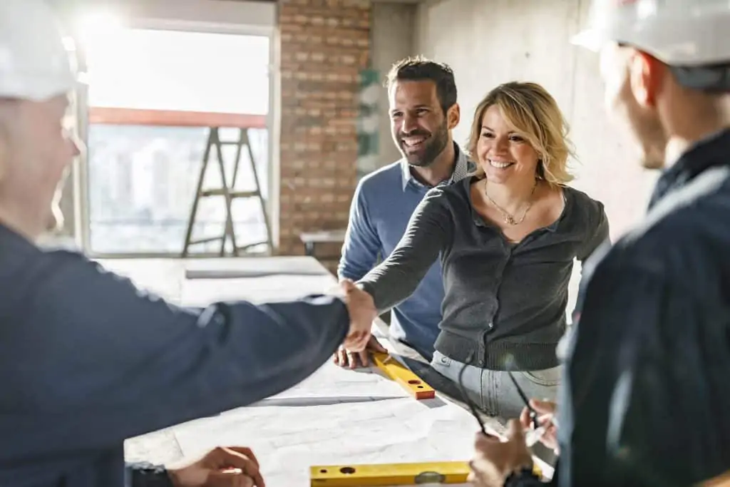 Happy couple came to an agreement with their building contractors at construction site. Focus is on woman.